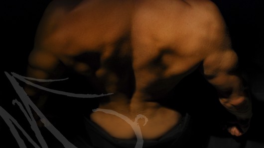 Fotografía del detalle de toda la musculatura de la espalda de un hombre dibujada bajo una luz de claroscuro