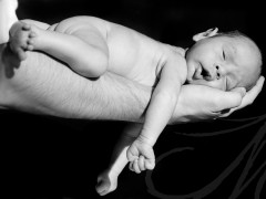 Fotografía en blanco y negro de un bebés desnudito sobre el brazo de su padre