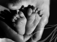 Fotografía detalle de los piececitos de un bebé de un mes entre las manos de su padre