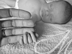 Fotografía detalle de la mano de una mamá agarrada por su bebé dormido, de fondo