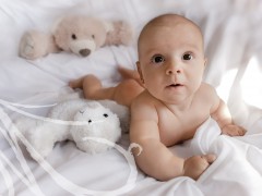 Fotografía de una bebé de cinco meses, sobre la cama, entre sus muñecos