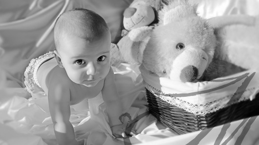 Fotografía en blanco y negro de un bebé a cuatro patitas junto a peluches